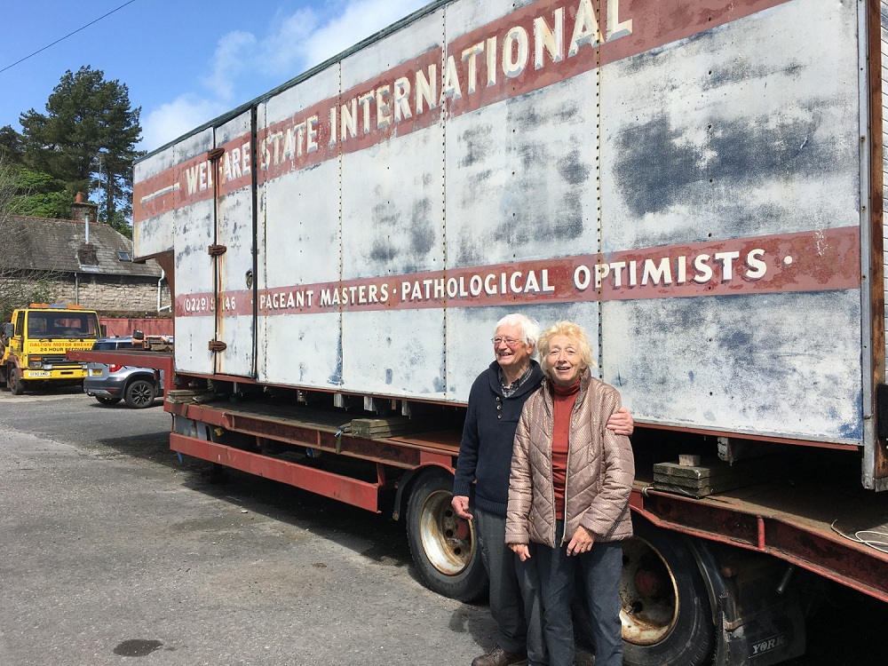 John Fox and Sue Gill standing in front of lorry trailer with the words Pathological Optimists painted on the side